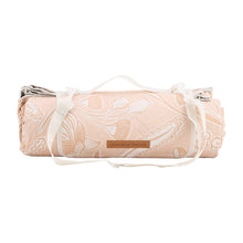 Load image into Gallery viewer, Tan/pinkish toned floral picnic mat shown rolled up and on a white background.