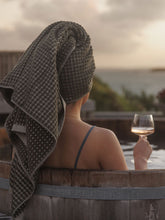 Load image into Gallery viewer, Person in a hot tub with a towel on their head, holding a glass of wine, with a scenic background.